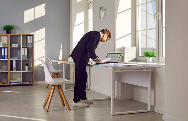 istock Accountant standing by his office desk, doing some paperwork, and using a laptop computer 2236627787