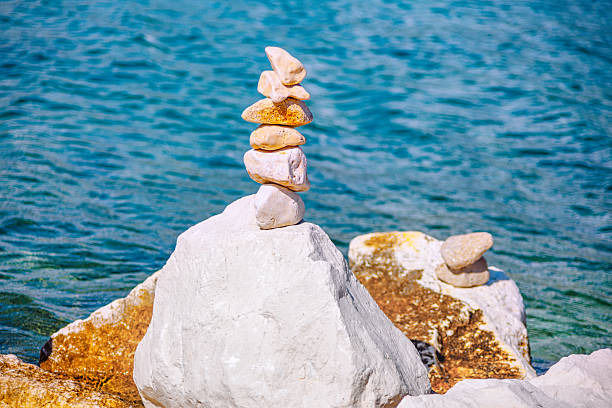 Perfectly balanced stone cairn stands resiliently against tranquil blue sea, symbolizing peace and harmony. Serene image offers calming touch for any project seeking natural beauty and quiet strength
