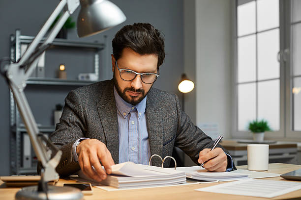 istock Male bookkeeper sitting at an office desk, doing paperwork, and reading documents 2236636729