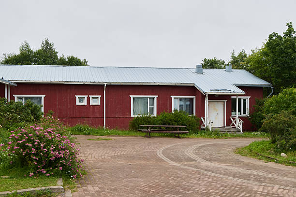 A charming red cottage with a lush garden and winding gravel path, set against a stunning cloudy sky