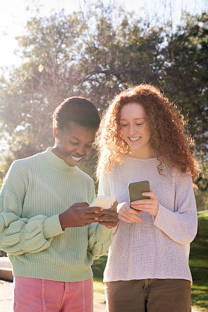 istock two women smiling and looking cell phone at park 2236640530
