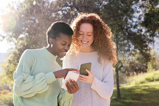 istock two young women looking mobile phone at park 2236640534