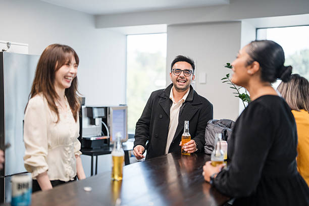 A team of professionals shares ideas in a modern office, holding glass bottles and expressing positive, enthusiastic emotions.