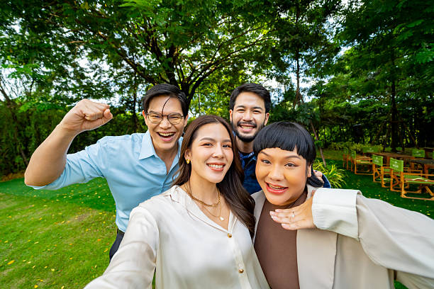 Group of Happy Diverse Asian millennial people friends using mobile phone taking selfie, enjoy holiday celebration social gathering dinner party outdoor festive event in garden evening together.