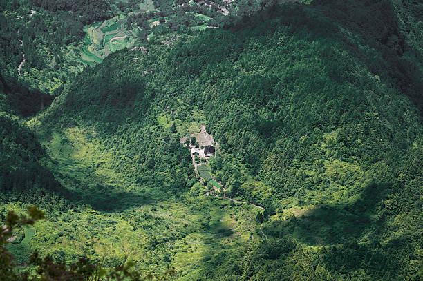 Remote house standing in a lush green valley surrounded by dense forest mountains