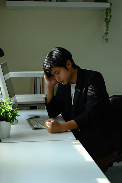 istock Young businessman at desk with hand on head, appearing tired and overwhelmed by workload 2236655376