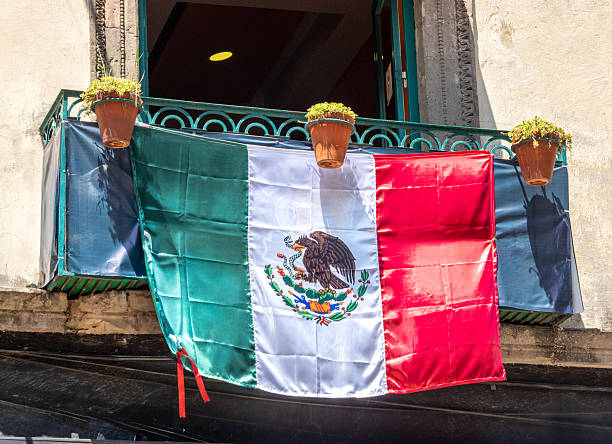 A flag with a green eagle on it hangs on a balcony. The flag is red, white, and green. Decoration to celebrate Independence Day in Mexico, zocalo