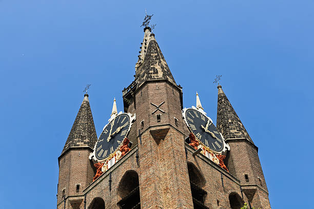 Upward view of the impressive Oude Kerk (Old Church) clock tower in Delft, Netherlands, with its historic spires reaching into the clear sky.