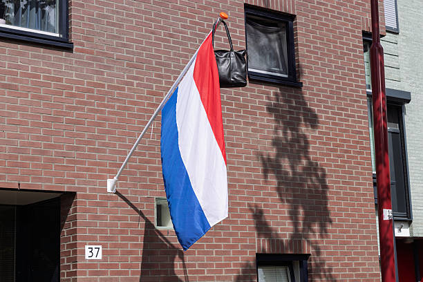 istock A Dutch flag hangs vertically from a brick building, with a black bag hanging from the top of the flagpole. 2236664769