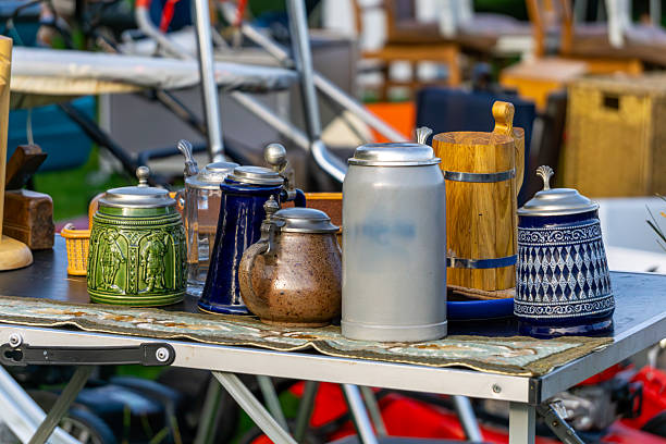Flea market with ceramic and metal beer steins and jugs displayed on table, featuring various patterns and colors.