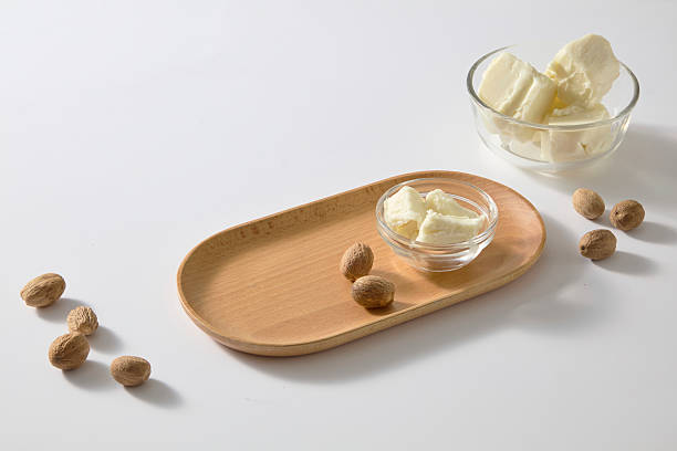 istock Wooden oval plate holding shea butter pieces next to loose shea nuts on plain white background, perfect for natural beauty or spa ingredient presentations. Copy space 2236672682