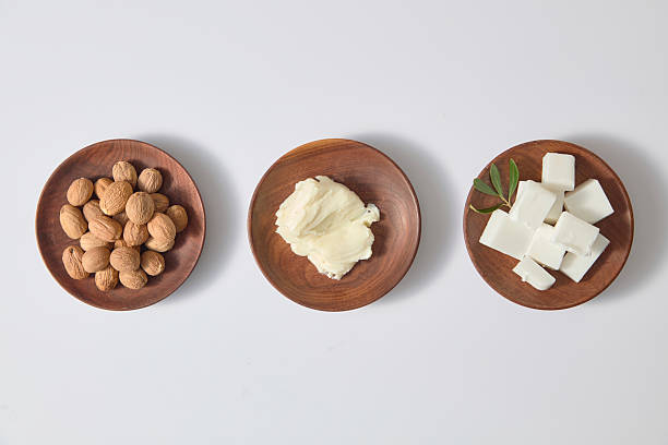 istock Three neat wooden bowls arranged with raw shea butter chunks and shea nuts on white tabletop, perfect clean layout for cosmetic or spa ingredient visuals. 2236672698