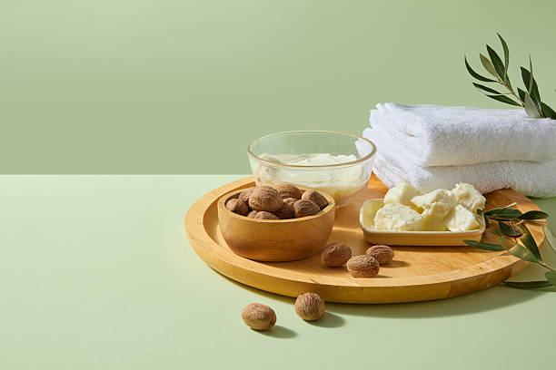 istock Rustic wooden tray holding ivory shea butter, scattered smooth shea nuts and soft sprigs on neutral fabric, ideal for handmade body butter or organic spa promotions. Front view, space for add text. 2236672913