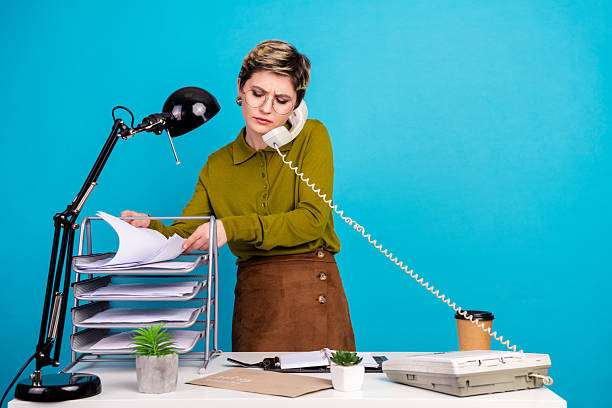 istock Young businesswoman multitasking at work in a retro styled office with documents on her desk and a phone in hand. 2236677450