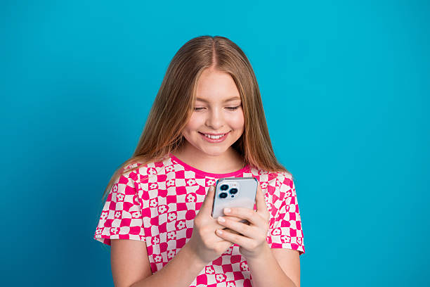 istock Adorable young girl using smartphone in a checkered shirt on a blue background, displaying cheerful emotions and casual style 2236678100