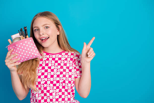 istock Young girl posing with polka dot makeup bag and gesturing against a bright blue background, promoting stylish cosmetics. 2236678145