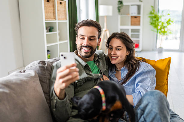 istock Smiling man and woman playing with their dog on couch using phone 2236680532