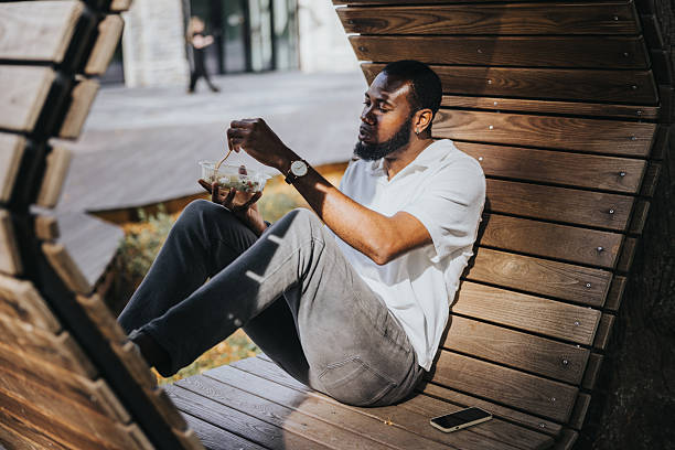 istock Black man eats take away salad in the public park during lunch 2236682824
