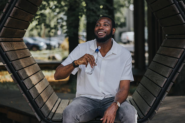 istock Black man drinks water from bottle in the park and smiles 2236682848