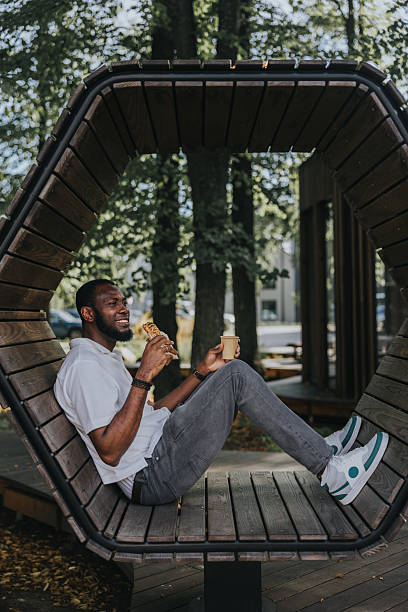 istock Black man eats pastry and drink coffee in the public park during lunch 2236682870