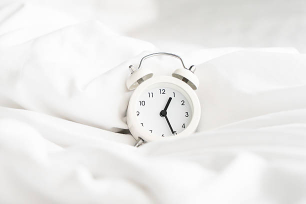 istock For late check out, wake up late concept, white analog alarm on comfortable  white bed, in soft focus 2236686534