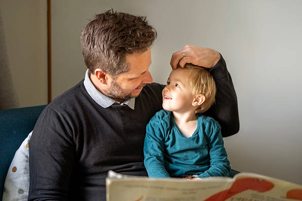 istock Loving father looking at toddler son while reading a book together at home 2236687334