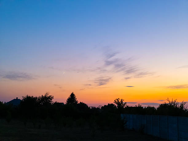 A view of a sunset with a crescent moon in the sky.