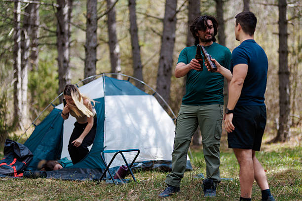 istock Friends enjoy camping adventure in the woods, sharing drinks and laughter while setting up their tent in a beautiful natural setting 2236693106