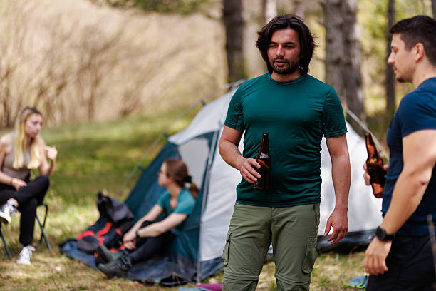 Friends enjoying a camping trip in a lush forest during a sunny day, sharing drinks and laughter near their tents, creating lasting memories together
