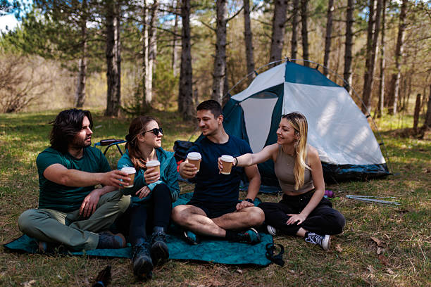 Friends enjoy a relaxing camping trip in the woods while sharing drinks and laughter during a sunny afternoon