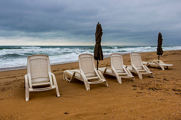 two deckchairs and a closed umbrella on a deserted beach at the end of summer with a dark and gloomy climate