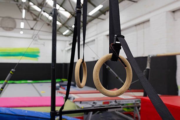 Close-up shot of two gymnastic rings suspended from the ceiling in a gymnastics club in North East England. There is various other equipment visible in the space.\n\nVideos similar to this scenario available.