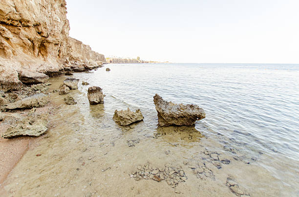 Tranquil seaside resort features rugged rocky shoreline under clear blue sky. Warm sunlight illuminates earthy tones of rocks, enhancing serene coastal atmosphere
