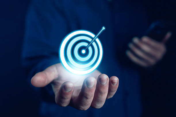 Hand holding glowing digital target with arrow hitting bullseye, symbolizing business goals, success, marketing strategy, achievement, focus, leadership, and future growth in modern technology.