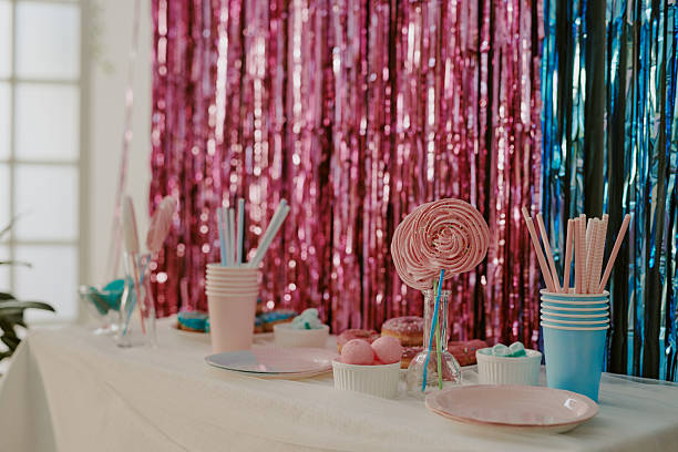 Candy buffet table displaying colorful sweets, lollipops, cups, plates, and treats arranged in front of shiny pink and blue tinsel backdrop, festive party celebration scene
