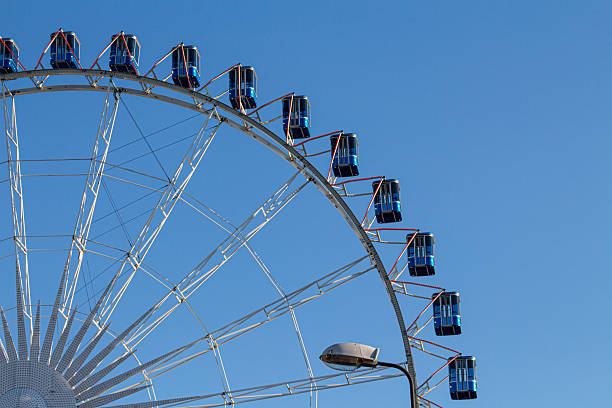istock Bright blue gondolas ascend on a large ferris wheel against a clear sky during a sunny day in the amusement park 2236704113