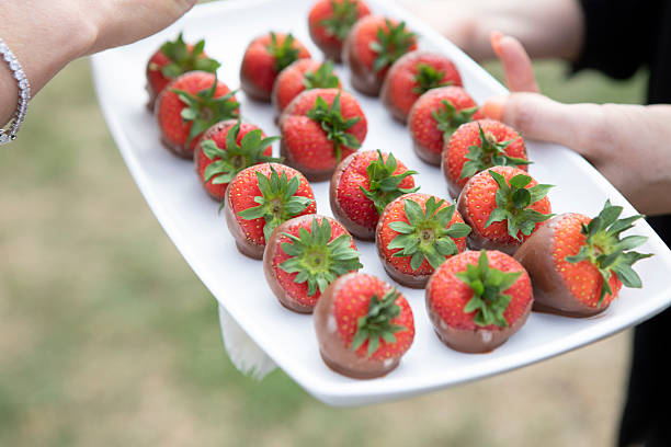 A person holding a tray of chocolate-dipped strawberries at an outdoor party
