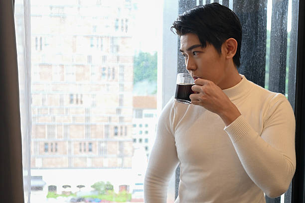 A young Asian man enjoys a peaceful moment at home with a warm cup of coffee.