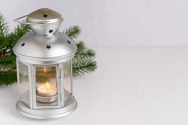 Festive christmas decoration with silver lantern with glowing lit candle light and fir tree branches on white wooden table with copy space prepared for winter holiday spirit celebration decor