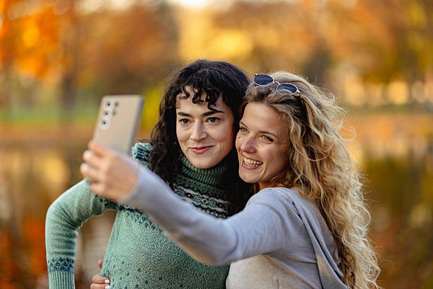 istock Friends enjoy a joyful moment together while taking selfies by a serene lake surrounded by colorful autumn foliage during a sunny afternoon 2236719333