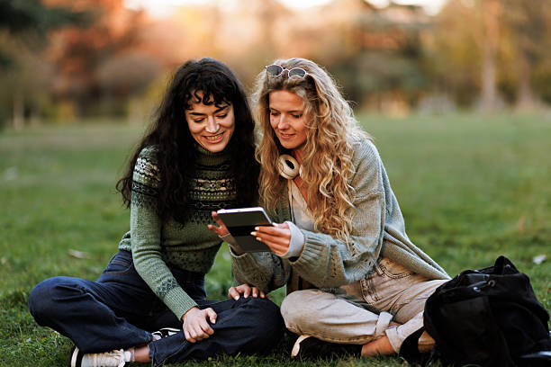 istock Two young women enjoy a sunny afternoon together in a park while looking at a mobile device, sharing smiles and laughter 2236719351