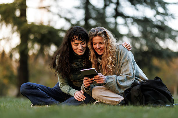 istock Friends enjoying a sunny day outdoors, sharing a moment with a tablet while seated on the grass in a park during the late afternoon 2236719368