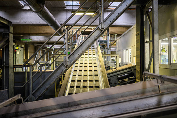 Industrial machinery is operating within an automated recycling plant featuring conveyor belts and waste sorting equipment. The facility is utilizing advanced technology for efficient waste management processes.