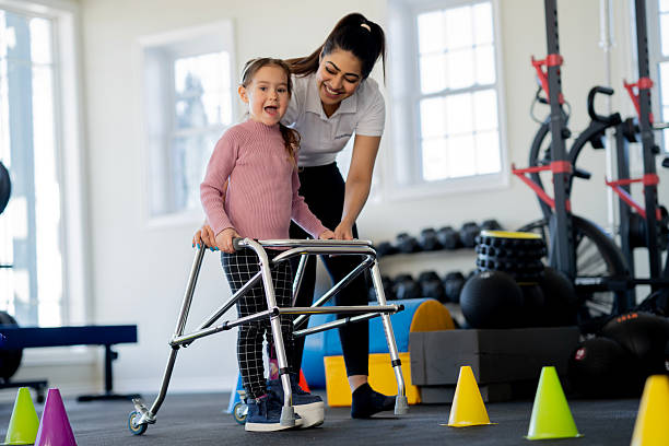 istock Young Girl With Limb Difference Using Walker Practicing Walking With Female Coach In Gym 2236729671