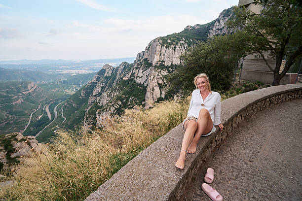 Woman sitting barefoot on a wall, enjoying the panoramic mountain view and valley.