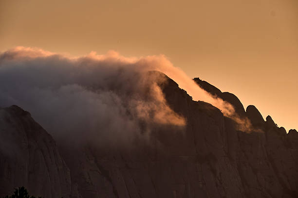 Golden hour light illuminating clouds flowing over a mountain ridge.
