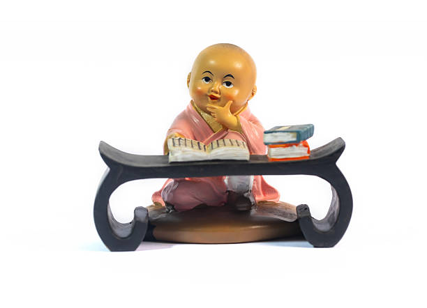 Charming statuette of a little novice monk from China in a thoughtful pose while reading. This souvenir, isolated on white, is a symbol of learning, peace, and contemplation