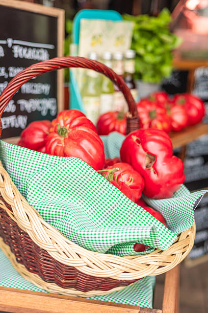Wicker basket with different types and shapes of fresh red tomatoes on white background.