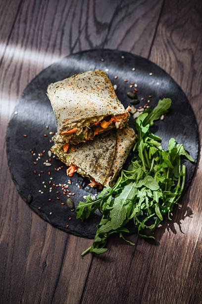 Delicious Homemade Tortilla Wrap Presented On Black Plate Alongside Fresh Crisp Rocket Salad
