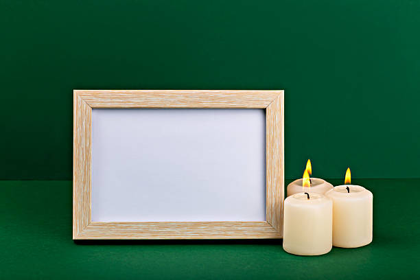 istock Wooden frame mock up with blank space beside lit candles on green background for design 2236737115